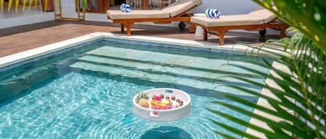 A clear swimming pool with lounge chairs and a fruit basket floating in the center.