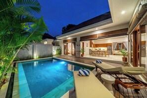 A modern outdoor pool area with lounge chairs, a dining area, and a kitchen visible through the glass doors. - Brand NEW Paradise Villa, Huge Pool, Canggu (Kabupaten Badung)