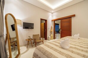 A hotel room with a bed, a chair, a small table, a mirror, a television, and a door leading to another room. - Brand NEW Paradise Villa, Huge Pool, Canggu (Kabupaten Badung)