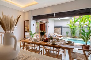 A dining area with a pool view, wooden furniture, and tropical plants. - Brand NEW Paradise Villa, Huge Pool, Canggu (Kabupaten Badung)
