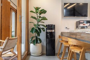 Eine moderne Küche mit Kühlschrank, einem Topfpflanzen, einem Esstisch mit Stühlen und einem an der Wand befestigten Flachbildfernseher.