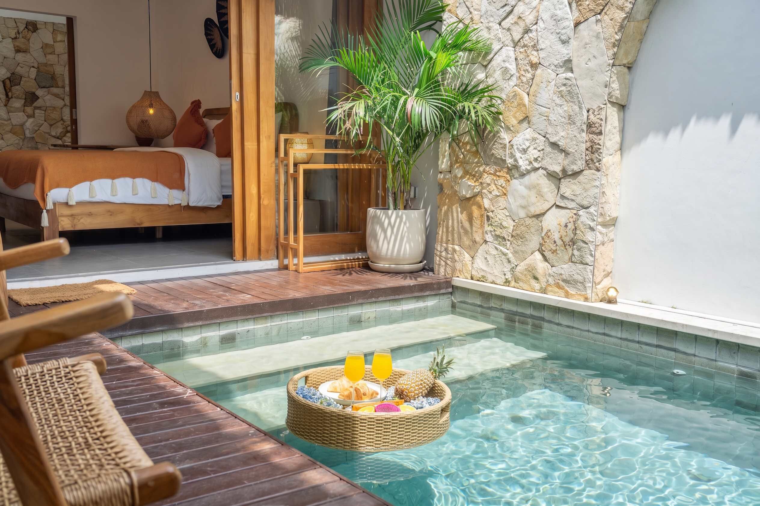 A pool area with a wicker basket containing food and drinks, a bed with a view, and a stone wall.