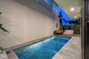 A swimming pool with a tiled deck, a wooden fence, and a seating area with a chair and a small table. - Brand NEW Villa+Amazing Jungle View+Huge Pool+4BDR (Kabupaten Badung)