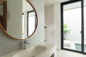 Ein modernes Badezimmer mit einem großen Spiegel, einem Waschbecken und einer Glastür, die auf einen Balkon mit einem Blumentopf führt.