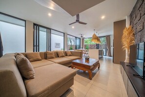Ein modernes Wohnzimmer mit einem Ecksofa, einem Holztisch und einem Fernseher auf einem schwarzen Standfuß.