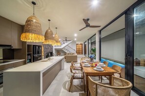 Eine moderne Küche mit Kochinsel, Essbereich mit Korbstühlen und Blick auf einen Pool durch eine Glastür.