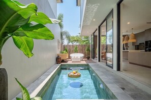 Ein moderner Innenpool mit einer schwimmenden Bar, einer Sitzecke mit weißem Sofa und einer durch eine Glastür einsehbarer Küche.