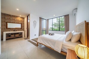 Ein modernes Schlafzimmer mit einem großen Bett, einem Schminktisch mit Spiegel und Blick auf Grünanlagen durch große Fenster.