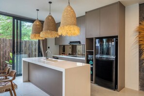 Eine moderne Küche mit Kochinsel, hängenden Pendelleuchten und einem Kühlschrank.