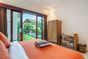 Een slaapkamer met een bed, een bureau, een kledingkast en uitzicht op een zwembad en tuin.