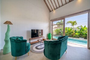 A modern living room with a large TV, teal chairs, a unique lamp, and a view of a swimming pool. - Brand New Paradise 2BDR Villa, Large Pool, Canggu (Kabupaten Badung)