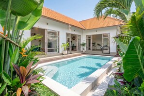 Een modern huis met een zwembad, grote ramen en tropische planten.