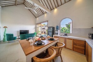 Eine moderne Küche mit Essbereich, Holzschränken, einem großen Fenster und Blick ins Grüne.