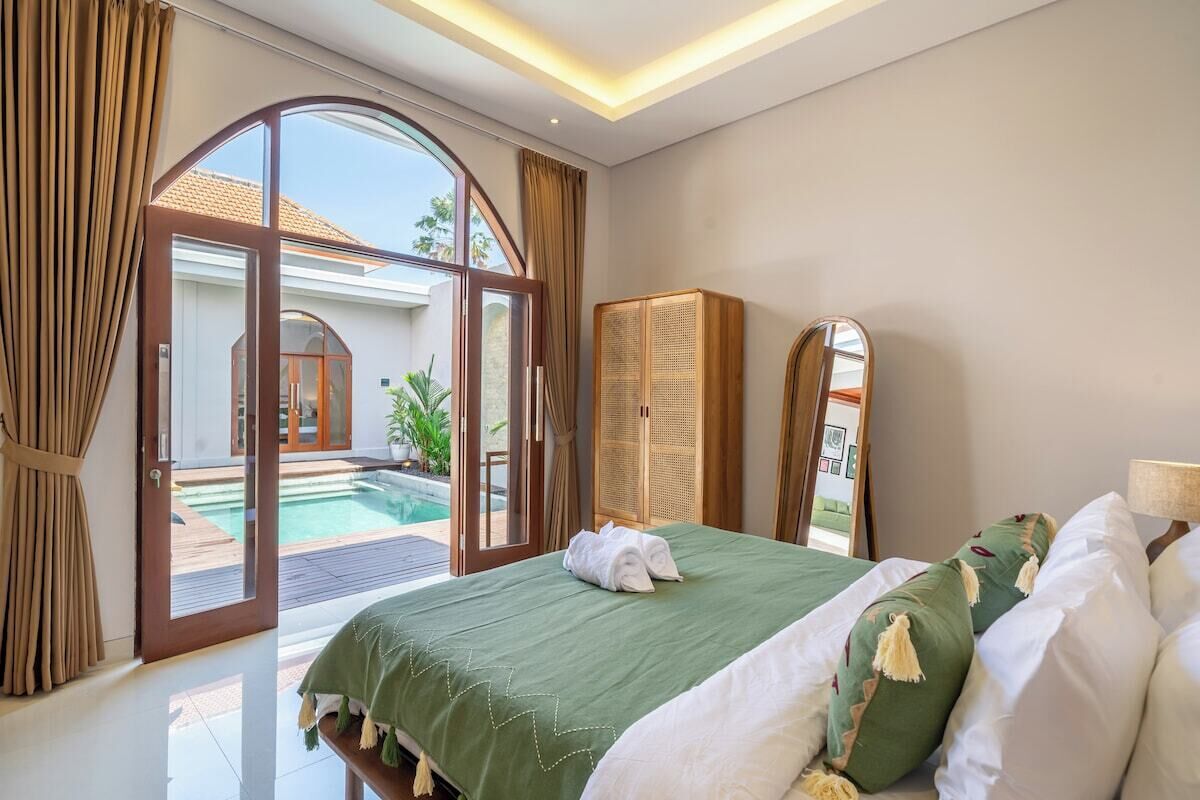 A hotel room with a bed, a large window, a view of a pool, and a mirror.