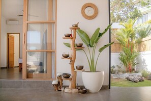 A modern interior with a wooden shelf holding bowls and a large potted plant. - Brand New 3 BDR Villa+Ricefield Views+Beach Access (Mengwi)