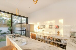 A modern kitchen with a marble countertop, a built-in oven, and a large window overlooking a garden. - Brand New 3 BDR Villa+Ricefield Views+Beach Access (Mengwi)