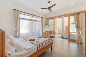 A bedroom with a bed, a ceiling fan, and a sliding glass door leading to a bathroom. - Brand New 3 BDR Villa+Ricefield Views+Beach Access (Mengwi)