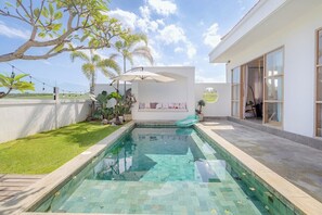 A swimming pool with a tiled deck, surrounded by a white wall and a grassy area with plants. - Brand New 3 BDR Villa+Ricefield Views+Beach Access (Mengwi)
