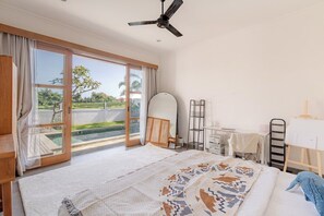 Een slaapkamer met een groot bed, een plafondventilator, een bureau en uitzicht op een zwembad.