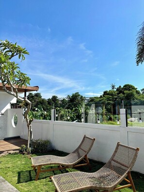 Two wicker lounge chairs on a grassy patio with a white wall and a tree in the background. - Brand New 3 BDR Villa+Ricefield Views+Beach Access (Mengwi)