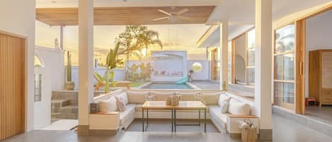 Un amplio salón con piscina, mobiliario y vistas a la puesta de sol.