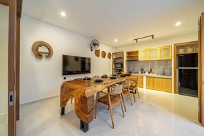 Eine moderne Küche mit einem langen Holztisch, Einbauküchenschränken und einem Flachbildfernseher.