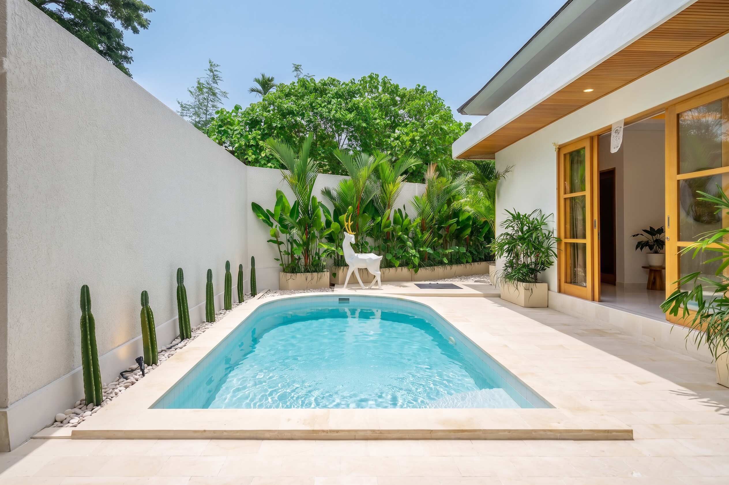 Une piscine rectangulaire dont le bord est recouvert de carreaux blancs, entourée d’un petit muret blanc et de différentes plantes.