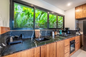 A modern kitchen with a large window, wooden cabinets, a black countertop, and a built-in oven. - Tropical 4BR Oasis w Huge Pool+Gazebo, Ubud's Best (Kabupaten Gianyar)