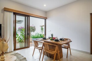 Ein moderner Essbereich mit Holztisch und Stühlen, eine Glastür zum Balkon mit Pflanzen und ein Fernseher auf der linken Seite.