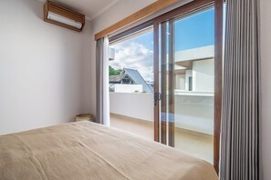 Un dormitori amb un llit, una porta corredissa de vidre que dona a un balcó i una finestra.