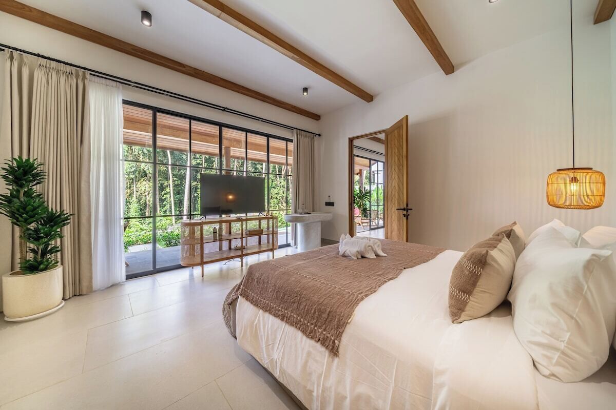 Ein geräumiges Schlafzimmer mit einem großen Bett, einem Fernseher und einem Balkon mit Blick auf Grünflächen.