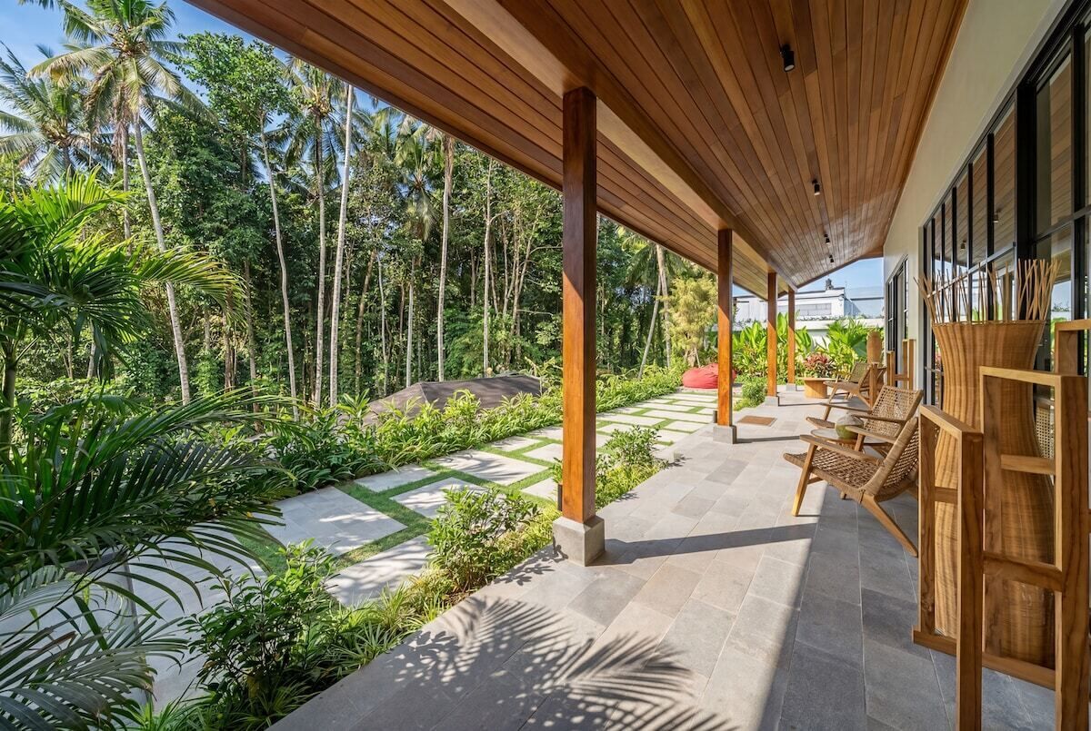 Un espace extérieur abrité, doté de piliers en bois, d’un chemin en pierre et d’une végétation luxuriante.