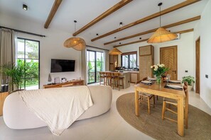 A modern living room with a sofa, dining table, and kitchen area. - Serene 2BR Escape in Prime Ubud - Pool+Lush Jungle (Kabupaten Gianyar)