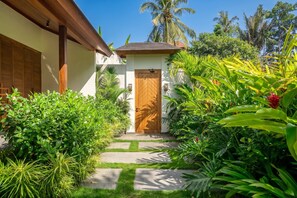 A tropical garden with a wooden door, lush greenery, and a clear sky. - Serene 2BR Escape in Prime Ubud - Pool+Lush Jungle (Kabupaten Gianyar)