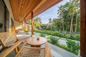 An outdoor seating area with wooden furniture and a view of a lush garden and palm trees. - Serene 2BR Escape in Prime Ubud - Pool+Lush Jungle (Kabupaten Gianyar)