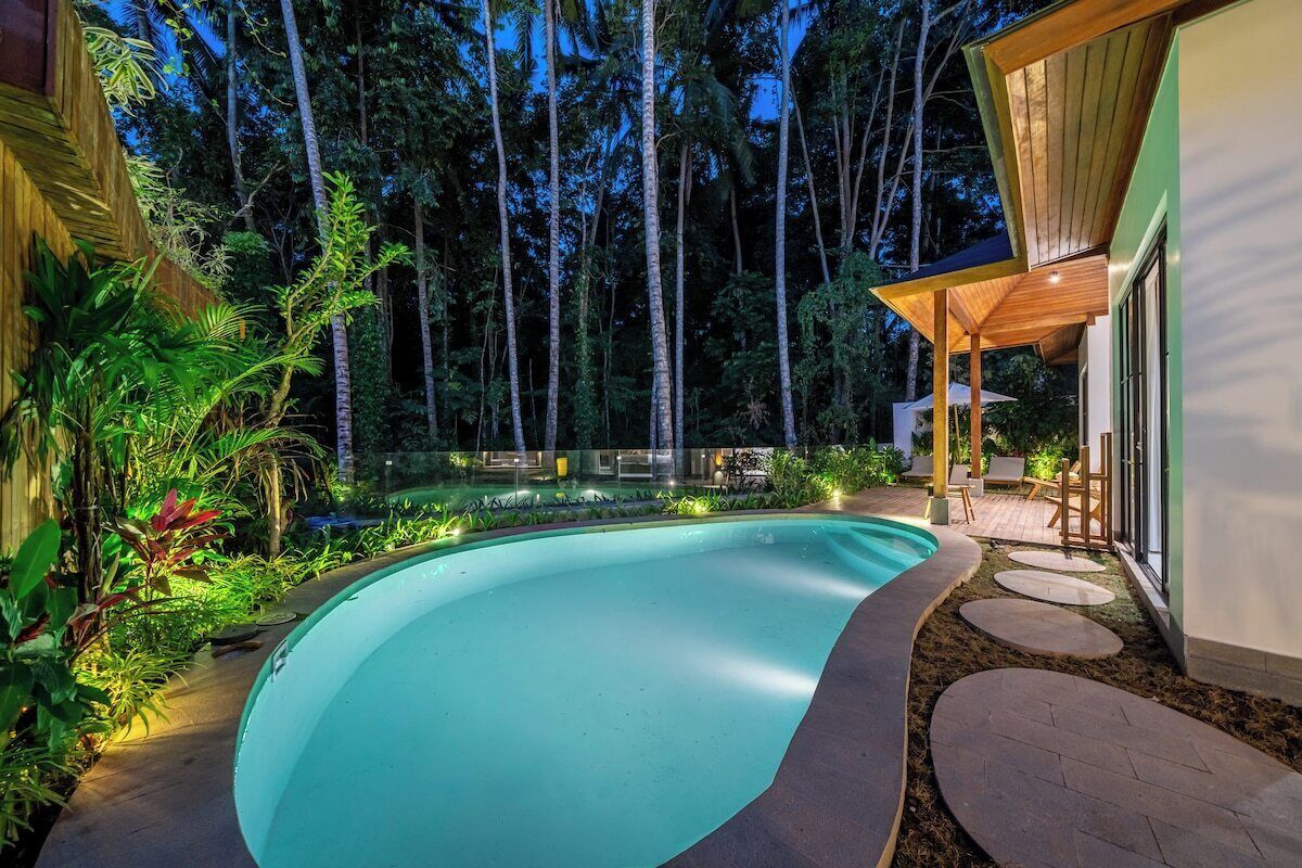 Une piscine à bordures courbes, entourée d’une terrasse en bois et d’un jardin luxuriant.