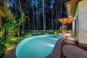 A swimming pool with a curved edge, surrounded by a wooden deck and a lush garden. - Serene 2BR Stay in Top Ubud's Spot w Pool & Garden (Kabupaten Gianyar)