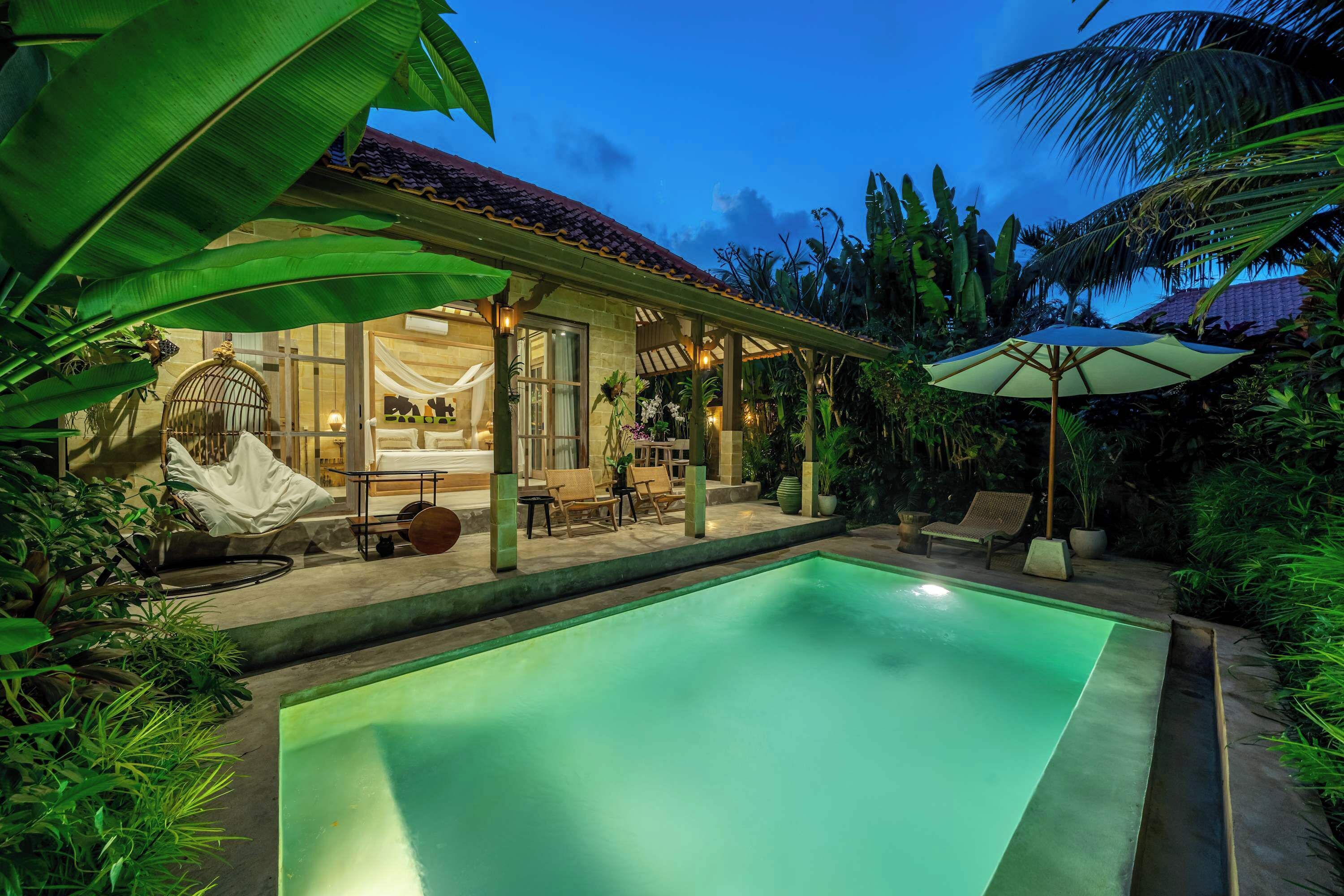 Un espace aménagé au bord de la piscine, comprenant un coin salon couvert, des chaises longues et une piscine bien éclairée.