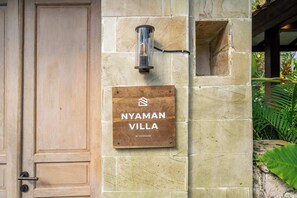 Eine Holztür und eine Steinwand mit einem Schild, auf dem 'NYAMAN VILLA' by Evdeki steht.