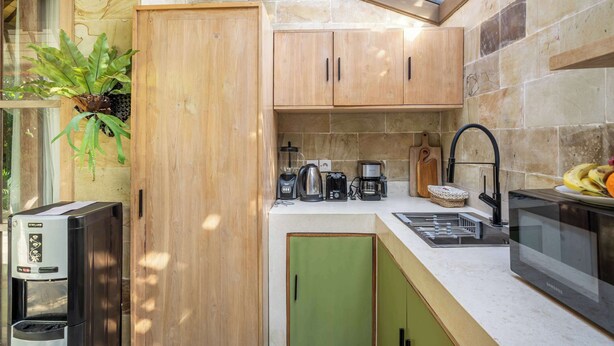 A compact kitchen with wooden cabinets, a coffee maker, a kettle, a microwave, and a sink. - Peaceful Ubud's 1BR • Lush Garden • Pool • Patio (Gianyar Regency)