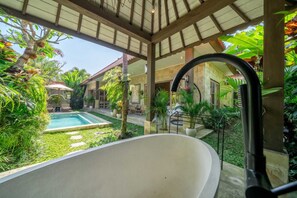 Un espace spa comprenant une baignoire sur pieds, une piscine et une végétation tropicale luxuriante.