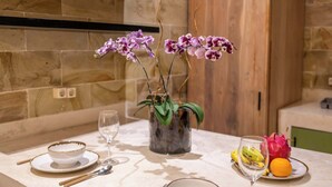 Een keuken met een marmeren aanrecht, een glazen vaas met paarse orchideeën, een fruitschaal met pitahaya en bananen, en een wijnglas.