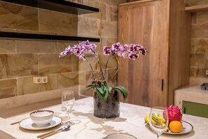 Eine Küche mit einer Marmarbele Arbeitsplatte, einer Glasvase mit violetten Orchideen, einer Obstschale mit Drachenfrüchten und Bananen sowie einem Weinglas.
