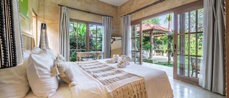 A spacious bedroom with a large bed, a ceiling fan, and a view of a garden through large windows.
