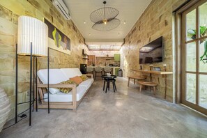 A modern interior with a stone wall, a white sofa, a dining area, and a TV mounted on the wall. - Serene Ubud 2BR Stay • Garden Bath • Private Pool (Ubud)