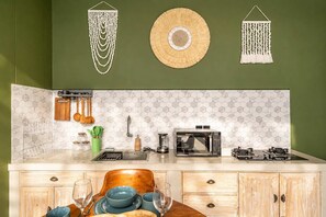 Una cocina con encimera blanca, microondas, estufa, utensilios colgantes y un salpicadero con estampado hexagonal.
