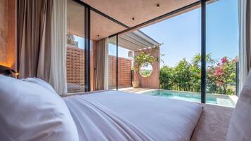 A bedroom with a large bed, a view of a swimming pool, and a brick wall.