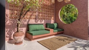 Et moderne udendørs opholdsområde med sofa, stor plantekasse og et rundt vindue med grønne planter.