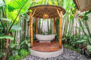 Eine runde Holzkonstruktion mit einer SteinsBadewanne in der Mitte, umgeben von tropischen Pflanzen und einem Steuboden.