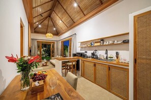 Een moderne keuken met houten kastjes, een eethoek met een houten tafel, en een uitzicht op een woonkamer.